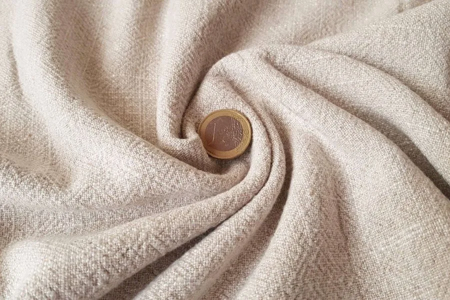 Nếp vải linen mộc màu kem cuộn quanh một nắp gỗ tròn